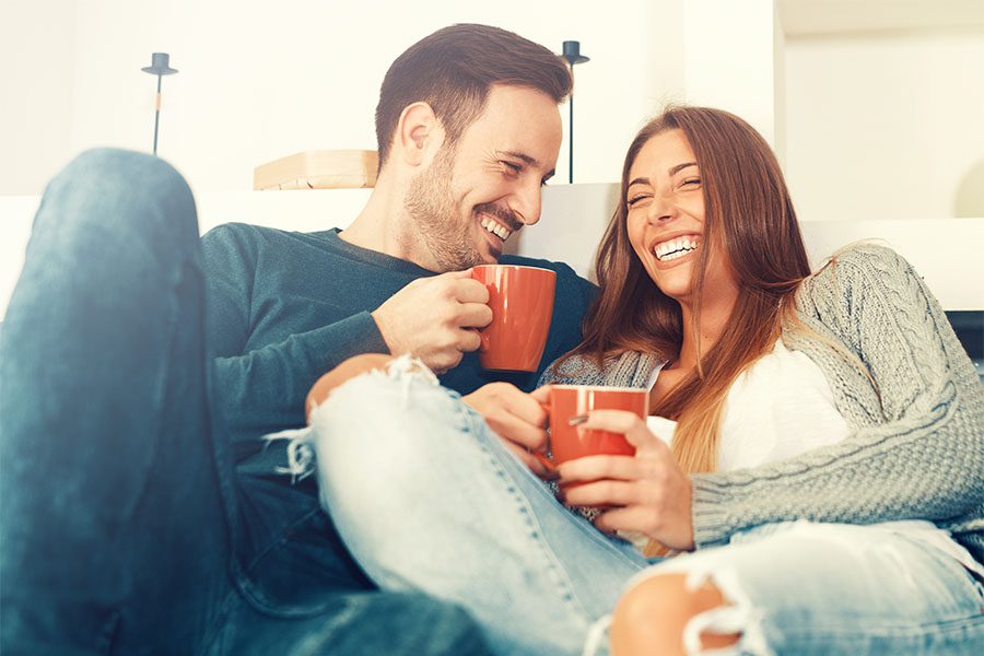 Client Center - Cheerful Young Couple Sitting at Home Enjoying a Cup of Coffee