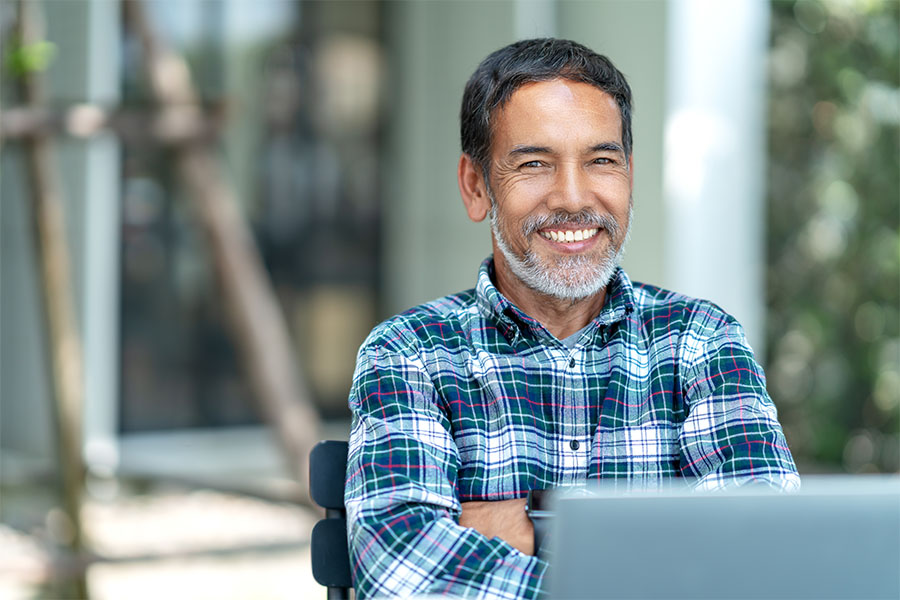 Insurance Quote - Smiling Mature Man Sitting Outside Using His Laptop